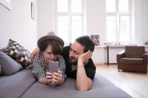 Eine junge Frau checkt ihr Smartphone, während ihr Freund sich mit ihr auf der Couch entspannt. — Stockfoto