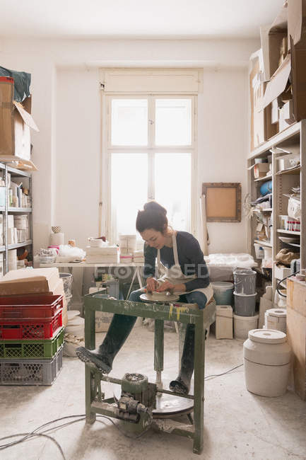 Mulher caucasiana está moldando argila de cerâmica em uma roda de cerâmica em uma oficina de cerâmica . — Fotografia de Stock