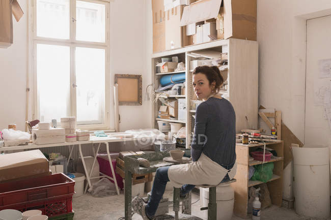 Mujer caucásica está dando forma a la cerámica de arcilla en una rueda de cerámica en un taller de cerámica . - foto de stock