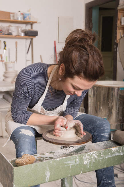 Caucasian woman is shaping pottery clay on a pottery wheel in a ceramic workshop. — Stock Photo