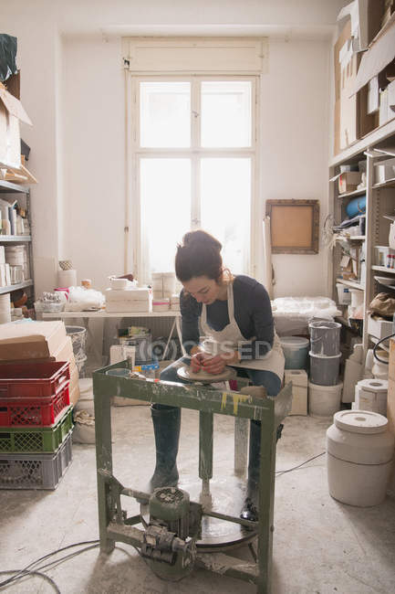 Mulher caucasiana está moldando argila de cerâmica em uma roda de cerâmica em uma oficina de cerâmica . — Fotografia de Stock