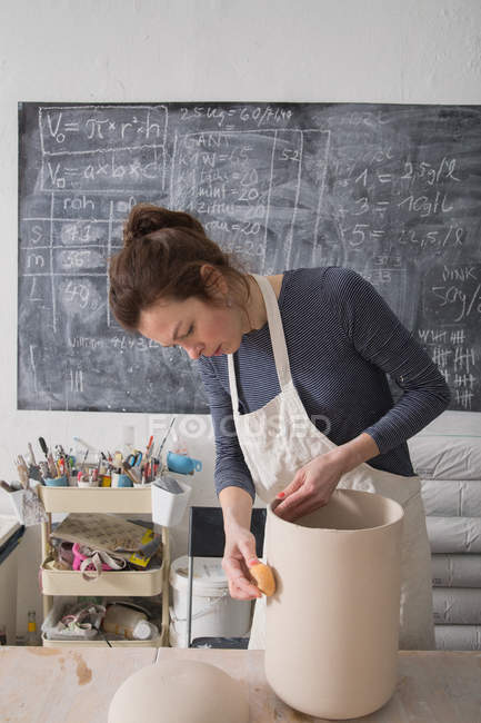 Un artista cerámico está dando los toques finales a una urna de cerámica en un taller de cerámica . - foto de stock