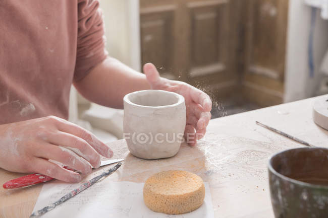 Um artista cerâmico está colocando os toques finais em uma xícara de cerâmica em uma oficina de cerâmica . — Fotografia de Stock