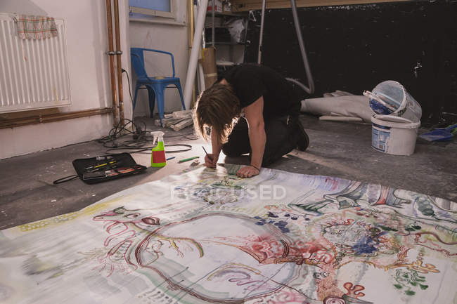 Творческий мужчина-художник работает в своей мастерской с живописью на полу — стоковое фото