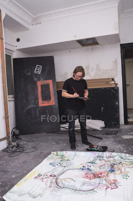 Творческий мужчина, работающий в мастерской с кистью в руке — стоковое фото