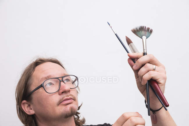 Retrato de artista masculino trabalhando em sua oficina e olhando para escovas nas mãos — Fotografia de Stock