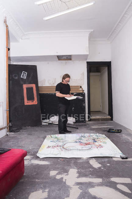 Творческий мужчина-художник работает в мастерской, держа в руках альбом эскизов — стоковое фото