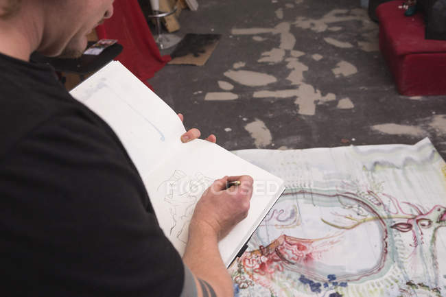 Creative male artist working in his workshop and painting in sketchbook — Stock Photo