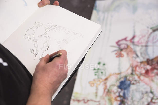 Kreativer männlicher Künstler arbeitet in seiner Werkstatt und malt in Skizzenbuch — Stockfoto