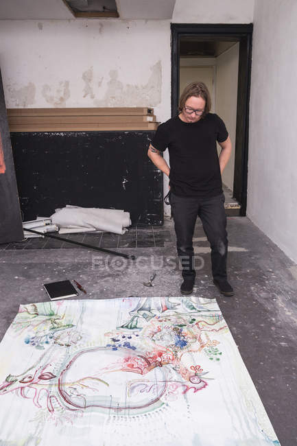 Kreativer männlicher Künstler, der in seiner Werkstatt arbeitet, während er auf Papier herabblickt — Stockfoto