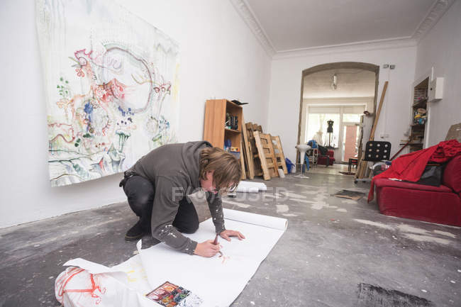 Artiste masculin créatif travaillant dans son atelier tout en s'agenouillant — Photo de stock