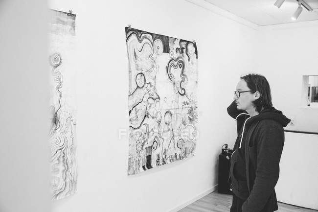 Schwarz-Weiß-Aufnahme eines kreativen männlichen Künstlers, der sein Kunstwerk in einer Kunstgalerie betrachtet. — Stockfoto