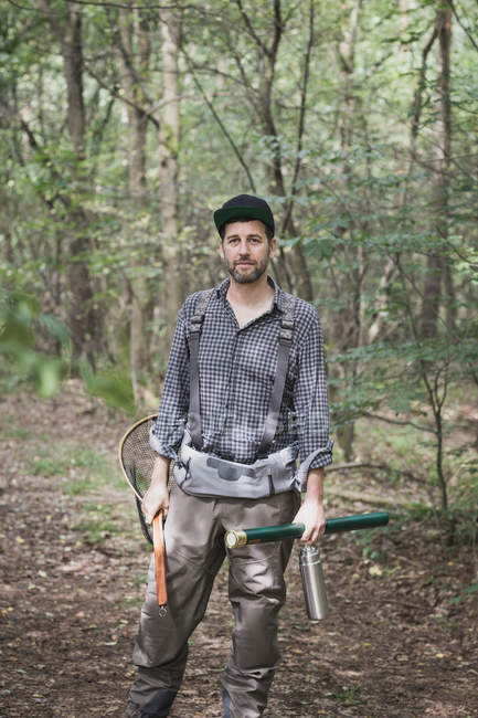 Front view of  man with fly fishing rod, landing net and waders in forest area. — Stock Photo