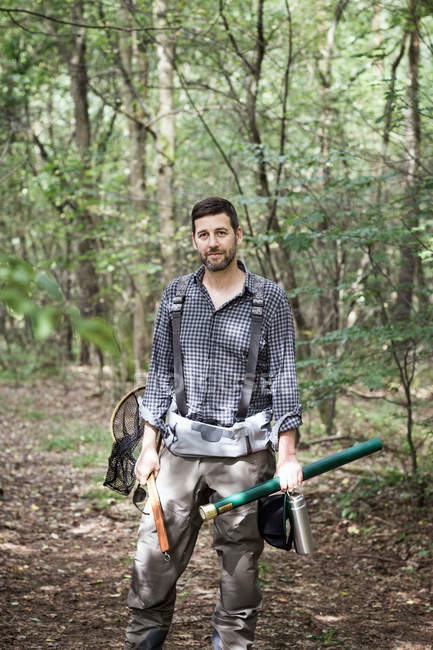 Front view of  man with fly fishing rod, landing net and waders in forest area. — Stock Photo