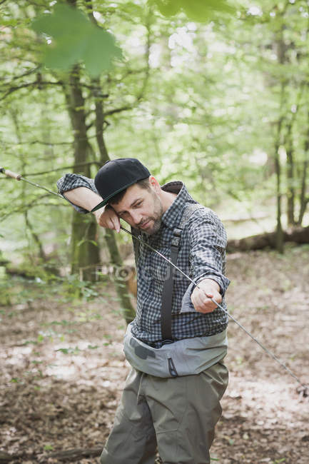 Un hombre está revisando su caña de pescar mosca en la zona forestal . - foto de stock
