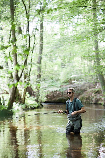 Ein Mann in Watstiefeln fischt auf Fluss in Waldgebiet. — Stockfoto