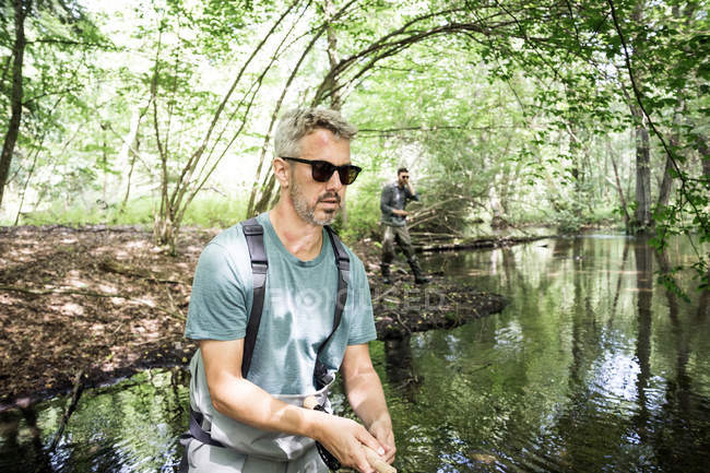 Zwei Männer in Watstiefeln fischen auf Fluss in Waldgebiet. — Stockfoto