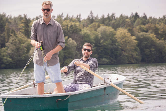 Человек гребёт на лодке, а его друг рыбачит с лодки на озере. . — стоковое фото