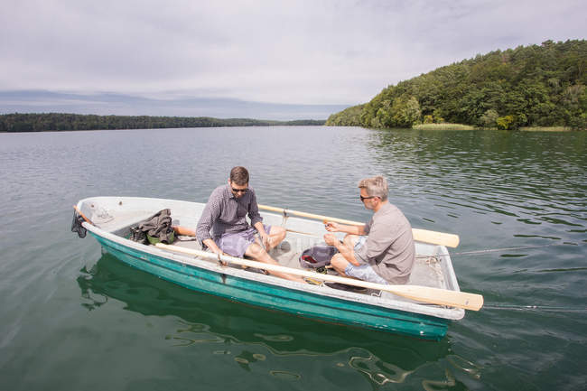 Dos hombres caucásicos en un bote de remos en el camino para hacer la pesca con mosca en el río . - foto de stock