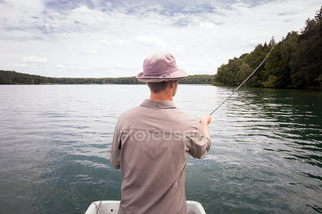 Rear view of man is fly fishing from boat on a lake. — Stock Photo
