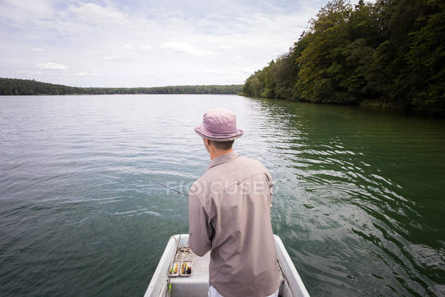 Vista posteriore dell'uomo è pesca a mosca dalla barca su un lago . — Foto stock