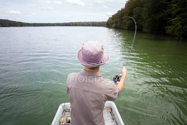 Visão traseira do homem é pesca com mosca de barco em um lago . — Fotografia de Stock