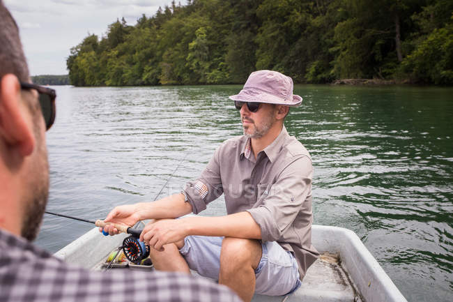 Um homem está remando um barco a remo, enquanto seu amigo é pesca com mosca de um barco no lago . — Fotografia de Stock