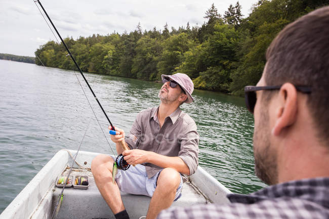 A man is rowing a rowboat while his friend is fly fishing from a boat on lake. — Stock Photo