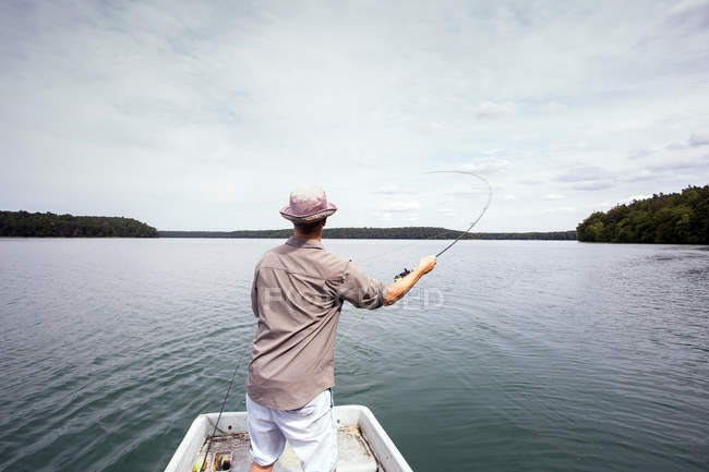 Un hombre es la pesca con mosca desde un barco en el lago . - foto de stock