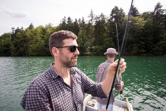 Los hombres caucásicos son la pesca con mosca en barco en el lago . - foto de stock