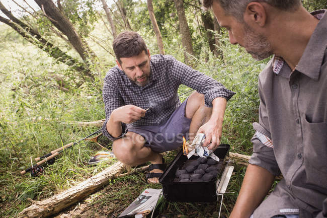 Dos hombres están preparando la parrilla para una barbacoa en plena naturaleza . - foto de stock