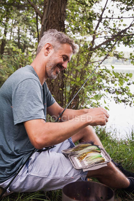 Un pescador está recogiendo una mosca de pesca de un aparejo de pesca con mosca . - foto de stock