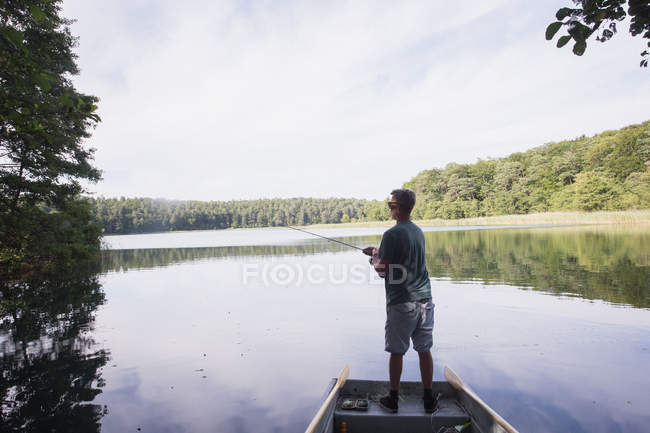 Rear view of man is fly fishing from boat on lake. — Stock Photo