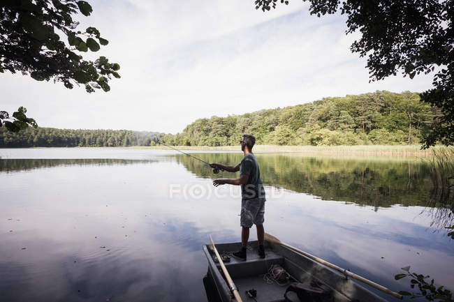 Rear view of man is fly fishing from boat on lake. — Stock Photo