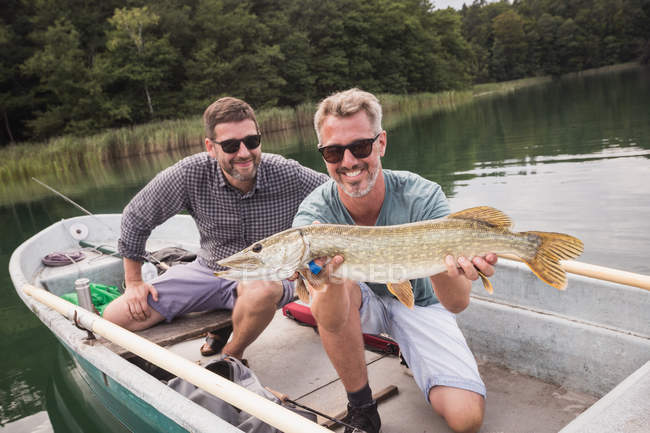 Two fly fishers are proudly showing a freshly catched pike from a boat on a lake. — Stock Photo