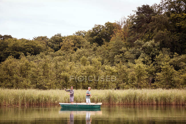Caucasian men are fly fishing in boat on lake against trees — Stock Photo