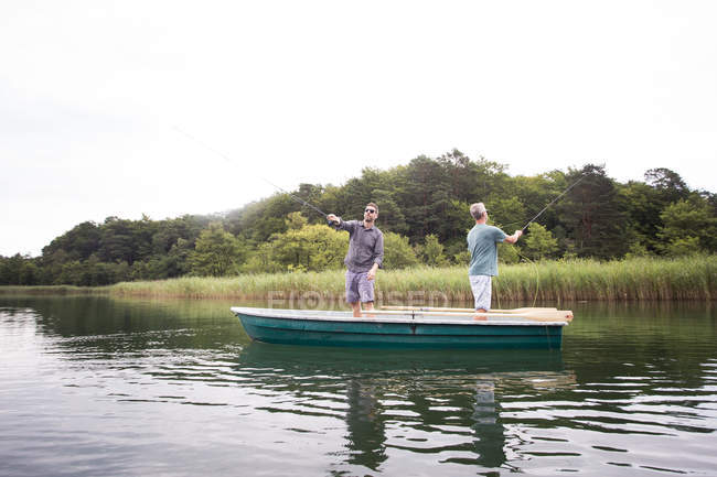Los hombres caucásicos son la pesca con mosca en barco en el lago durante el día - foto de stock