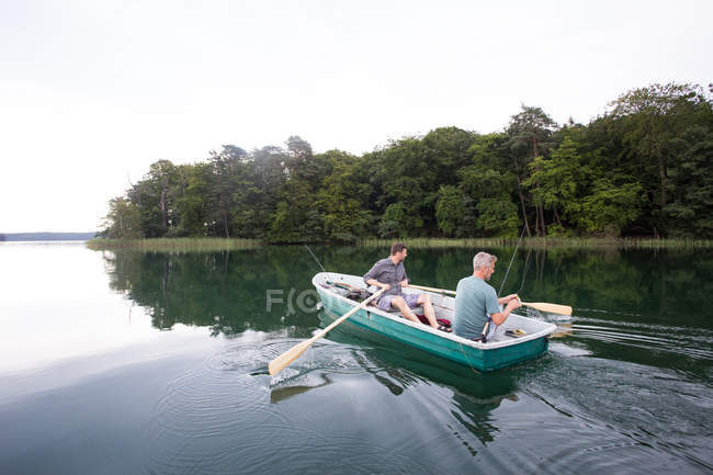 Чоловік веслує на човні, а його друг летить на риболовлю з човна на озері . — стокове фото