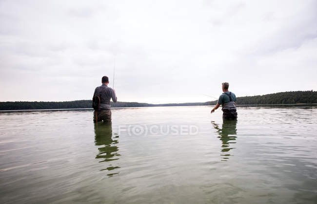 Rückansicht zweier Männer in Watstiefeln beim Fliegenfischen in einem See im Morgengrauen. — Stockfoto
