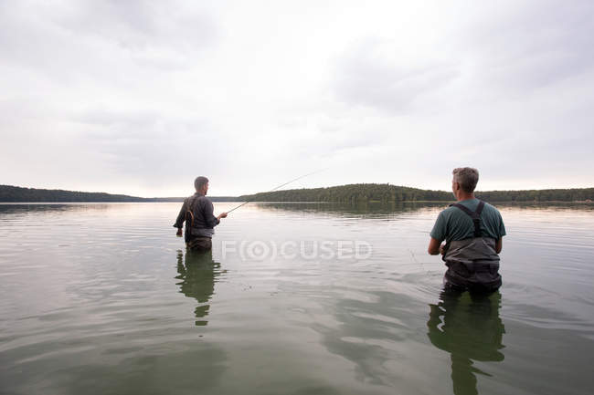 Vue arrière de deux hommes dans des échassiers pêchent à la mouche dans un lac à l'aube . — Photo de stock