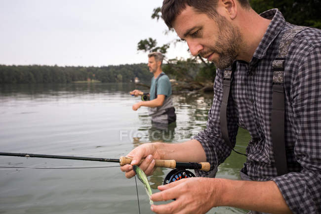 Vista lateral de dois homens em waders são pesca com mosca em um lago ao amanhecer . — Fotografia de Stock