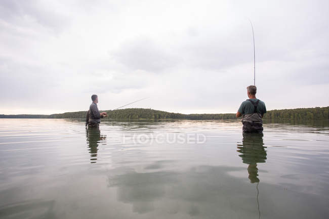 Dos hombres en waders son la pesca con mosca en un lago al amanecer . - foto de stock