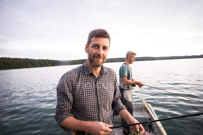 Gli uomini caucasici sono pesca a mosca in barca sul lago durante il giorno — Foto stock