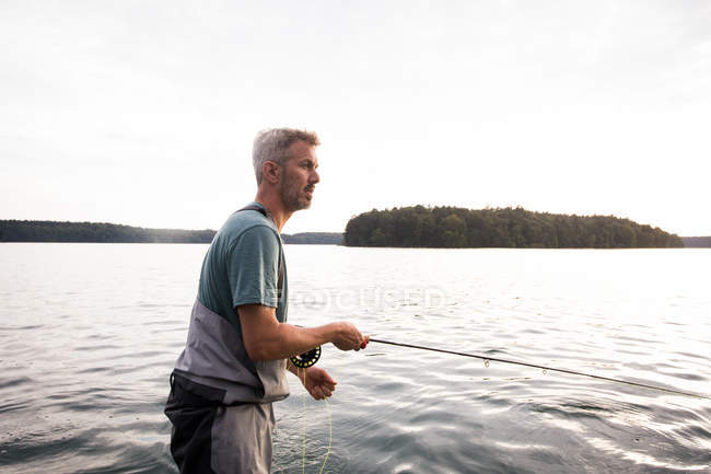 Vista lateral do homem em waders é a pesca com mosca de um barco no lago . — Fotografia de Stock