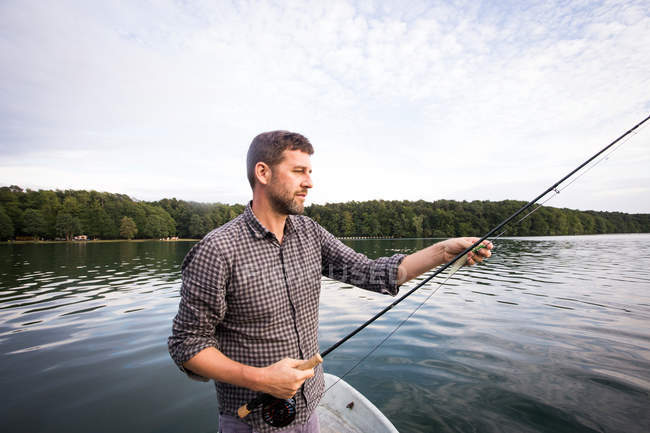 Vista lateral del hombre es la pesca con mosca desde un barco en el lago . - foto de stock