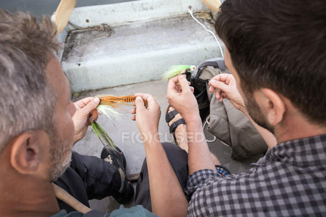 Two men are picking a fishing fly from a fly fishing tackle in boat on river. — Stock Photo
