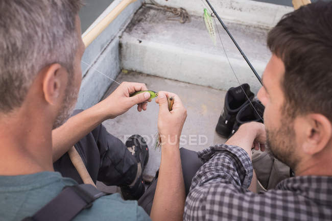 Zwei Männer pflücken eine Fliege von einem Fliegenfischergerät in einem Boot auf dem Fluss. — Stockfoto