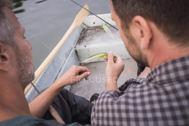 Two men are picking a fishing fly from a fly fishing tackle in boat on river. — Stock Photo