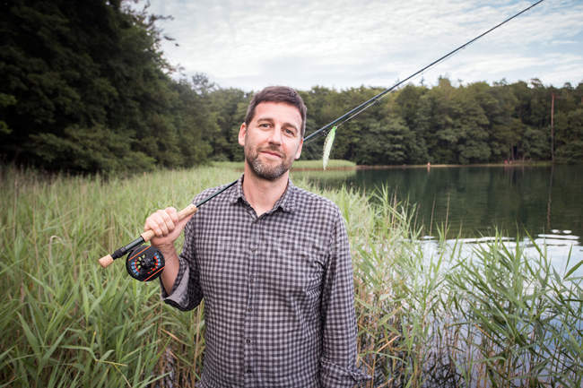 Content Caucasian fly fisher with his fishing rod at a lake. — Stock Photo