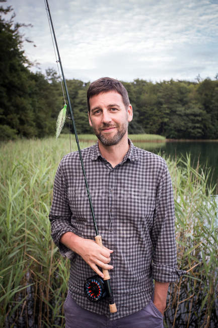 Smiling Caucasian fly fisher with his fishing rod at a lake. — Stock Photo